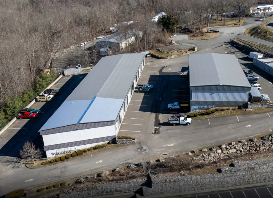 United Flex New Fairfield from the air: two metal buildings and their parking below a wooded hillside